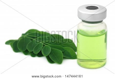 Moringa leaves with extract in a vial over white background