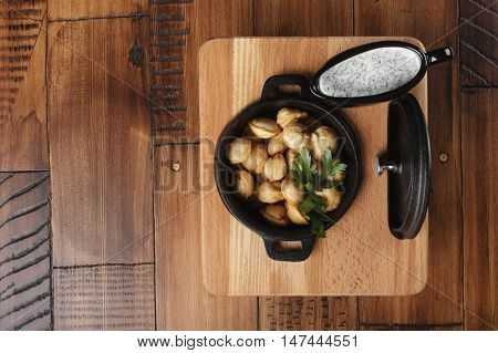 Fried meat dumplings (pelmeni, chuchpara) in a black pan. wooden background.