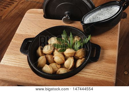 Fried meat dumplings (pelmeni, chuchpara) in a black pan. wooden background.