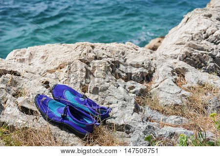 Pair of violet water shoes on the rocks on coast of the sea.