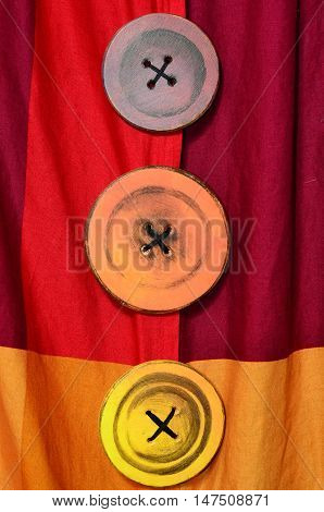 Three colorful buttons / pins / knobs in a column on red and orange fabric