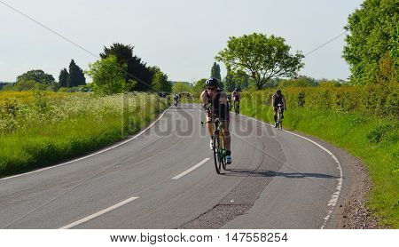 Grafham, Cambridgeshire, England - May 22, 2016:  Triathletes on road cycling stage of triathlon fields and trees in background.