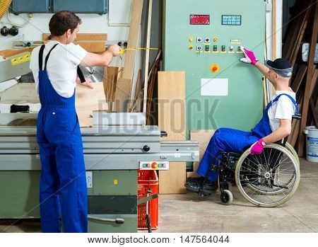 Worker In Wheelchair In A Carpenter's Workshop With His Colleagu