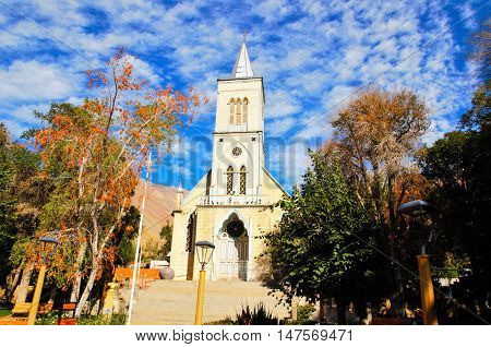 Low angle view of the church in Pisco Elqui with trees on eather side and a blue sky with some white clouds in the Elqui Valley in Chile, South America
