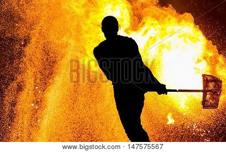Fireshow performance. Silhouette of man with hammer, fire around