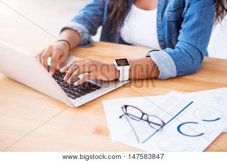 Involved in work. Pleasant woman sitting at the table and using laptop while working on the project
