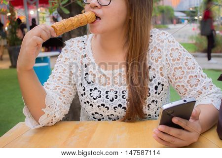 asia woman play moblie phone and eat quick meal Chicken Roll Cake or Gai Jor