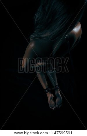 Low key photo of sexy female nude back and hands binded with cuffs and collar holding whip against dark background overhead view