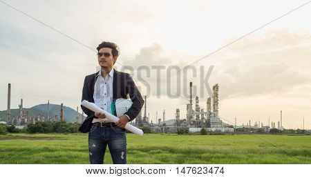 refinery engineer with white safety helmet see drawing standing in front of oil refinery building structure in heavy petrochemical refinery industry.