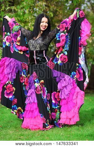Young happy woman in beautiful skirt zingara stands on lawn outdoor