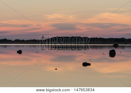 Evening sunlight lighthouse and rocks on coast. Sky reflection on water. Beach in summer. Seaside natural environment. Shore in Osmussaar Island Nature Reserve in Estonia National Park in Europe