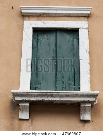 Old window with closed shutters with flowers on the window sill on the stone wall. Italian Village.