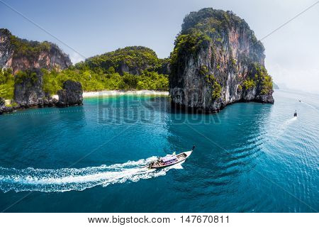 Aerial view of clear sea with traditional longtail thai boats and the rocky mountains on the background