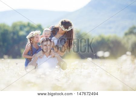 Happy family of four,mother,father,older sister and little brother spend time together in the highlands on a field of blooming white daisies in summer in the fresh air,mother and daughter wearing wreaths of flowers-white daisies