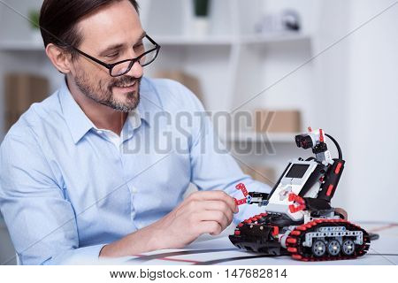 Good mood. Middle-aged white man in glasses fixing a small robot.