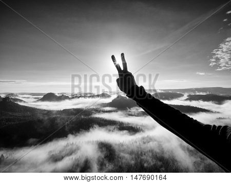 Man hand make victory to Sun. Misty daybreak in a beautiful hills. Peaks of hills are sticking out from foggy background. Black and white photo