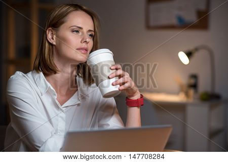 Mull over it. Pleasant beautiful concentrated woman sitting at the table and thinking while drinking coffee