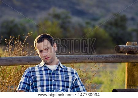 Man with a bored, indifferent expression slouching sitting in a field.