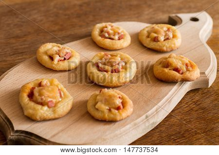 Mini pizzas with sausage and cheese on cutting board on wood table.