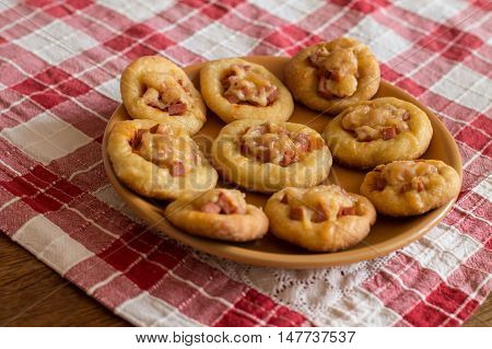 Mini pizzas with sausage and cheese in orange plate on checkered tablecloth.