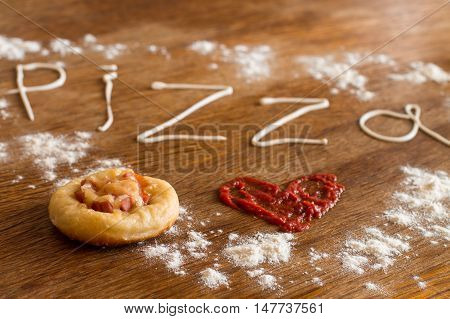 Mini pizza with sausage and cheese on wood table. Painted heart of ketchup, written text 