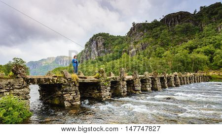 Tourist woman standing on stone slab bridge Terland Klopp in Norway Dalane region.