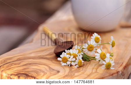Chamomile tea with chamomile daisy flowers in a hot white cup on a wooden rustic cutting board and a spoon. This home remedy is known to help sleep and aid a sore throat