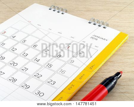 close-up white cardboard desk calendar with days and date of January 2016 page and red marker pen on brown wooden table, reminder monthly business planning or task scheduler