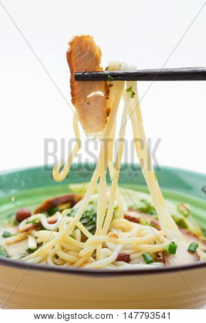 picking up piece of bbq prok with chopsticks from bowl of guilin rice noodles on white