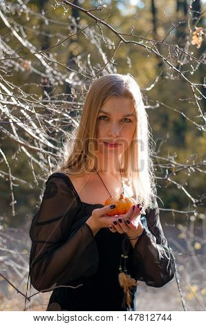Portrait Of A Young Long-haired Blond Girl In A Black Dress Posing With A Pumpkin