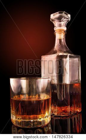 Glass with a decanter on a black surface with reflection against the background of a gradient. Vertical format. Color. Photo.