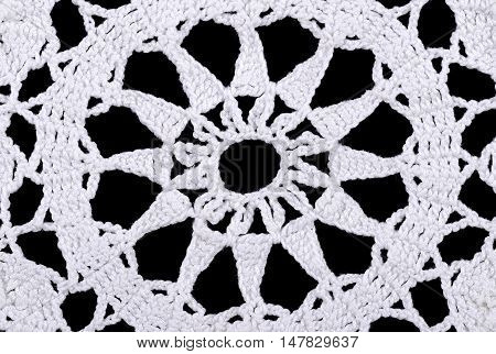 Star in a white crocheted doily. Crochet is a process of creating fabric by interlocking loops of yarn  using a crochet hook. Macro photo close up from above on black background.