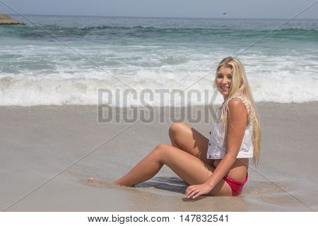 A sexy blonde female with a revealing bikini outfit that are the colours of the American flag with the beach in the background