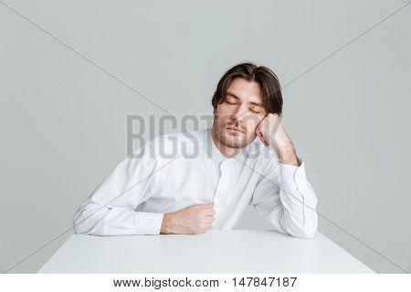 Hadsome young man in white shirt sleeping while sittng at the desk isolated on the gray background