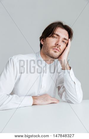 Young man in white shirt sleeping while sittng at the desk isolated on the gray background