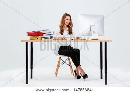 Beautiful happy businesswoman using computer while sitting at the desk at office isoltaed on the white background