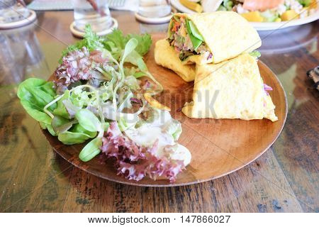 Egg rolls with salad and fresh vegetble on wood plate