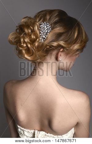 Portrait of a young girl from the back with the collected hair from the curls and silver comb in white dress with open shoulders