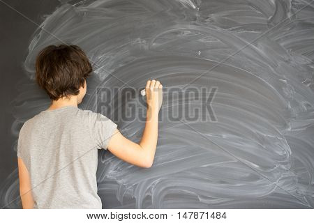 Boy with chalk in hand writting on empty blackboard