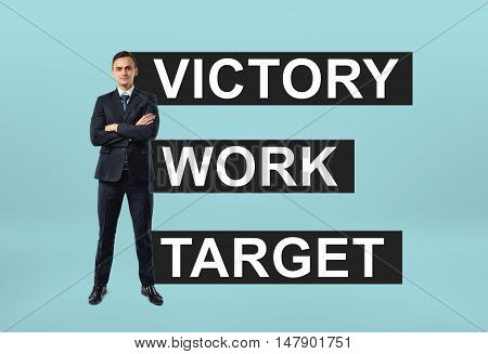 Front view of a businessman standing confidently with a motto 'victory work target' behind him. Successful lifestyle. Management and administration.