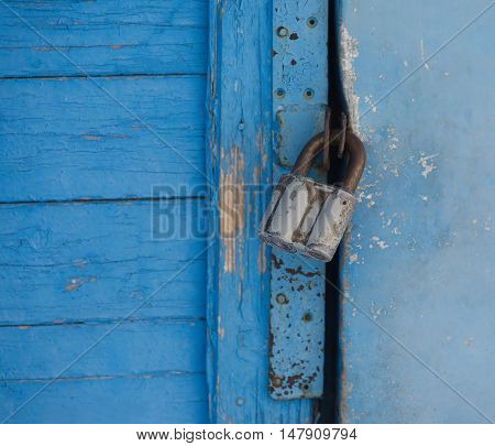 Gray metal lock hangs on a blue painted door closeup