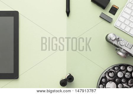 Work space on green table of a creative designer or photographer with laptop tablet camera and other objects of inspiration and copy space. Stylish home studio concept of technology trends. View from above.