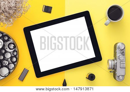 Work space on yellow table of a creative designer or photographer with blank tablet camera and other objects of inspiration and copy space. Stylish home studio concept of technology trends. View from above.