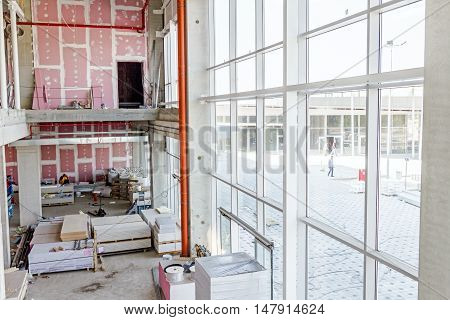 View on indoor construction site of unfinished modern large showroom with gypsum wall and huge windows.
