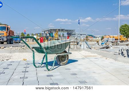 Dirty wheelbarrow is at building site. New pavement is made of cobblestone blocks still under construction.
