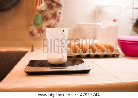 Cup of milk staying on scales on kitchen table closeup.