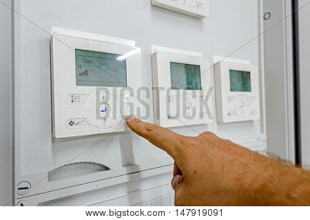 Hand is pushing button operating to climate control panel which contains a digital display for temperature check to residential place.