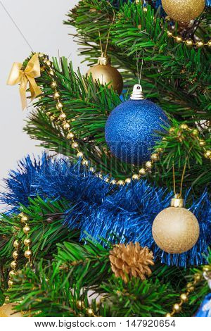 Christmas decorations on a green artificial fir. Golden and bright blue on a green background. Fragment. Photo with limited depth of field.