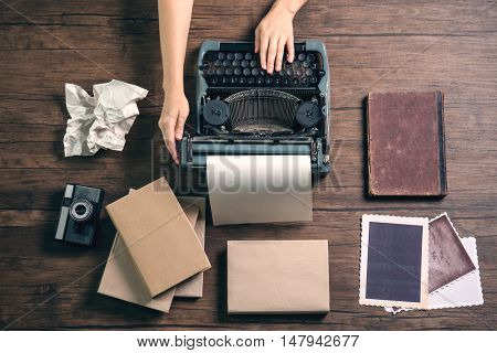 Woman hands working with retro typewriter, camera and photos on wooden background