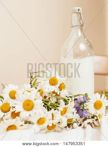 Simply stylish wooden kitchen with bottle of milk and glass on table, summer flowers camomile, healthy foog moring concept close up
